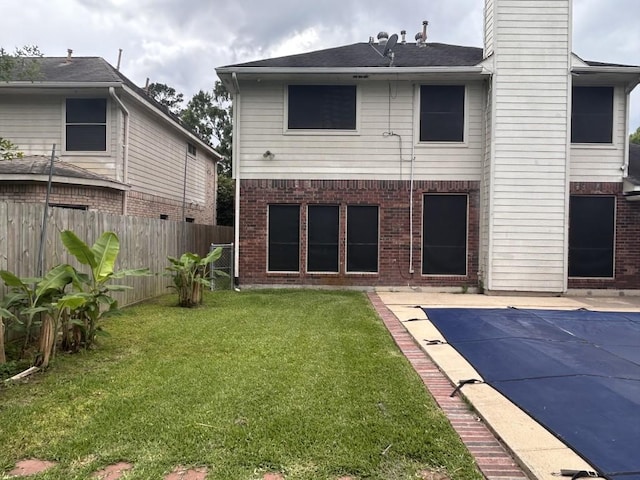 rear view of house featuring fence, brick siding, a fenced in pool, a chimney, and a yard