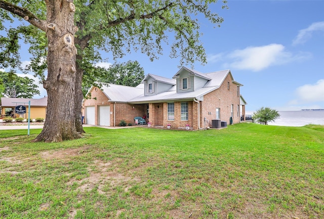 view of front of house with a garage, a front yard, brick siding, a water view, and central air condition unit