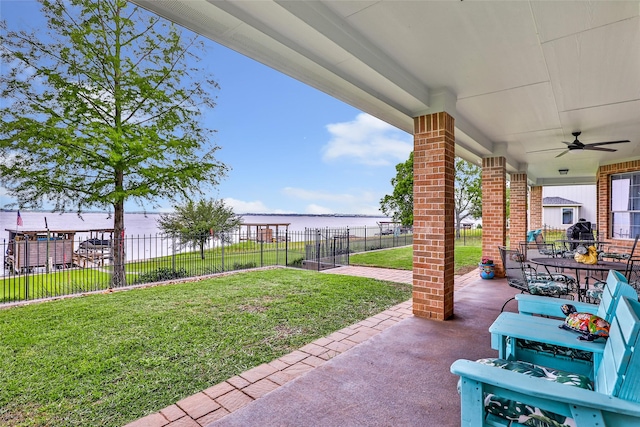 view of yard with fence, outdoor dining area, a ceiling fan, a patio area, and a water view