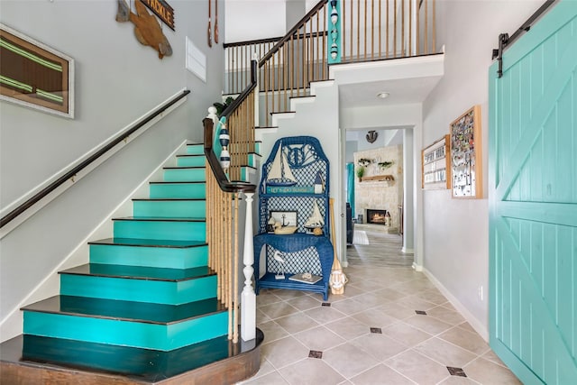 stairway featuring tile patterned flooring, a towering ceiling, baseboards, a stone fireplace, and a barn door