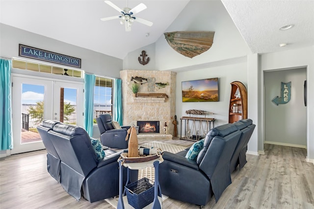 living area featuring a fireplace, high vaulted ceiling, french doors, a ceiling fan, and light wood-style flooring