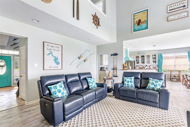 living room featuring light wood-style floors, baseboards, and a towering ceiling