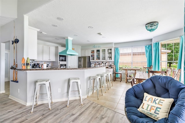 kitchen featuring a breakfast bar area, freestanding refrigerator, a peninsula, island exhaust hood, and glass insert cabinets
