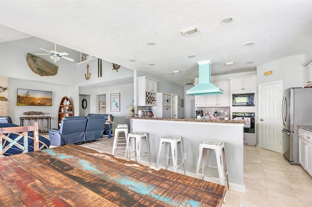kitchen featuring ceiling fan, ventilation hood, dark stone counters, visible vents, and black appliances
