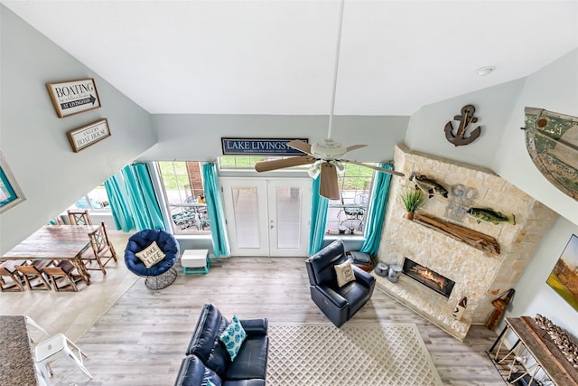 living area featuring a ceiling fan, vaulted ceiling, a stone fireplace, and wood finished floors