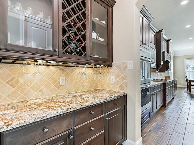 kitchen with glass insert cabinets, dark brown cabinetry, light stone countertops, and stainless steel appliances