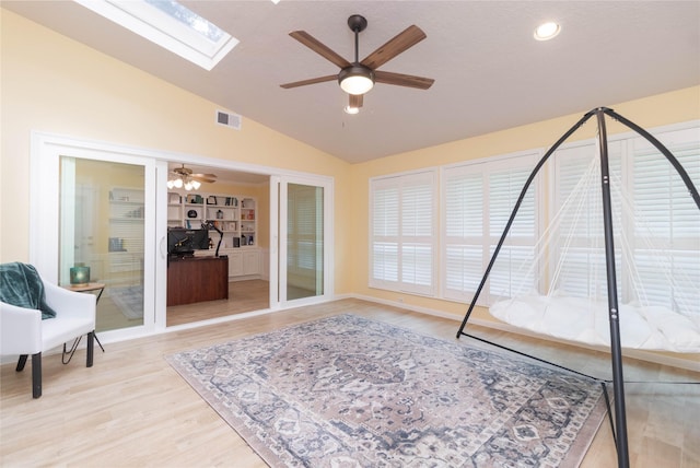 interior space with light wood-type flooring, a ceiling fan, lofted ceiling with skylight, and visible vents