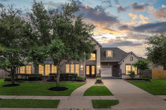 view of front of home featuring fence, brick siding, a gate, concrete driveway, and a lawn