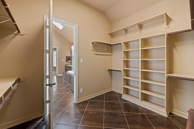 spacious closet featuring dark tile patterned floors and vaulted ceiling