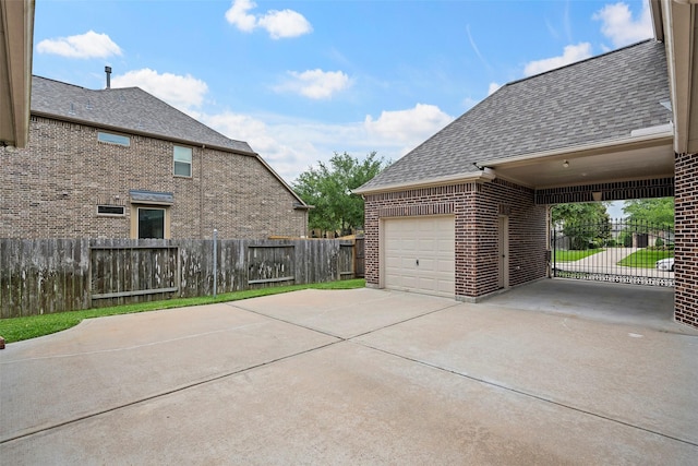 exterior space with driveway, brick siding, fence, an attached garage, and a shingled roof