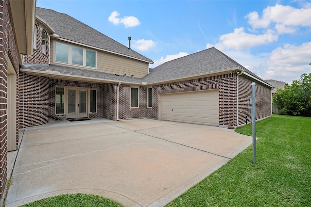 rear view of house with an attached garage, brick siding, french doors, a yard, and driveway