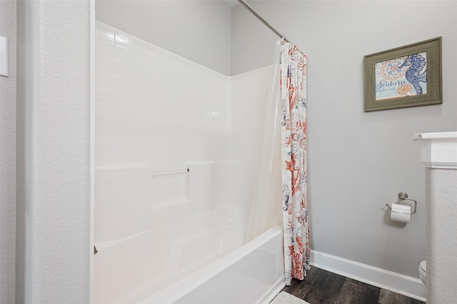 bathroom with wood finished floors, baseboards, shower / bath combo with shower curtain, and toilet