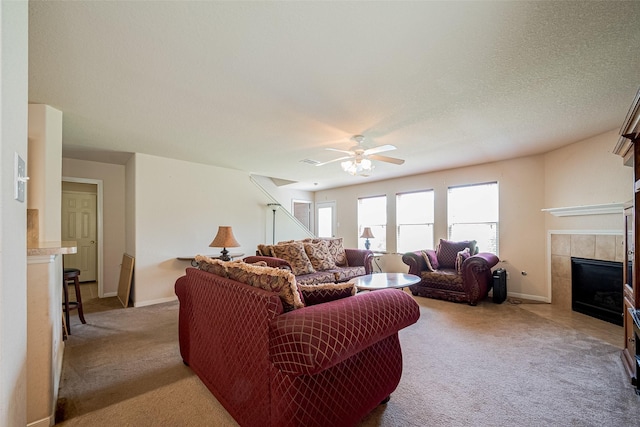 living area featuring a ceiling fan, baseboards, light colored carpet, and a tiled fireplace