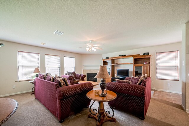 living area featuring a ceiling fan, visible vents, a fireplace, baseboards, and light carpet
