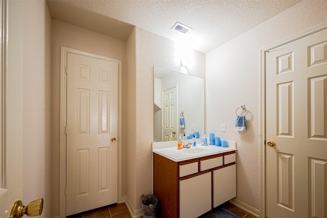 bathroom with a textured wall, vanity, a textured ceiling, tile patterned floors, and visible vents