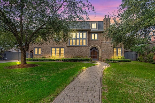 tudor house featuring fence, a chimney, brick siding, and a front yard