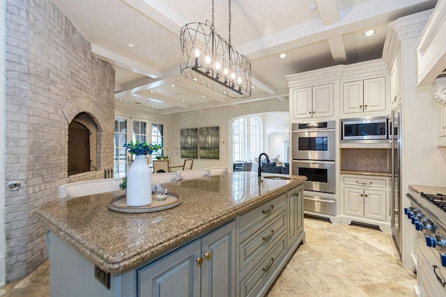 kitchen with appliances with stainless steel finishes, a sink, open floor plan, a warming drawer, and coffered ceiling