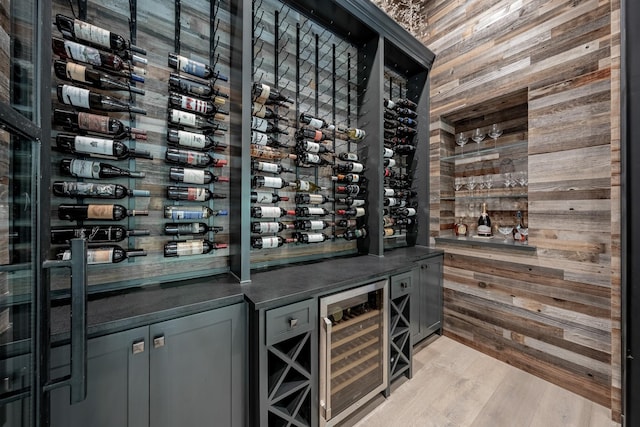 wine area with beverage cooler, wood walls, and light wood-type flooring