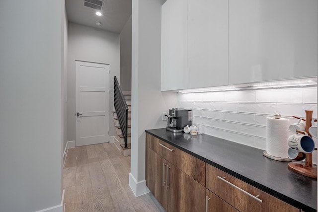bar featuring visible vents, stairs, baseboards, tasteful backsplash, and light wood-style flooring