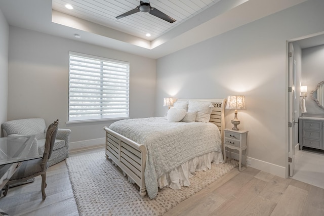 bedroom with recessed lighting, a raised ceiling, baseboards, and light wood finished floors