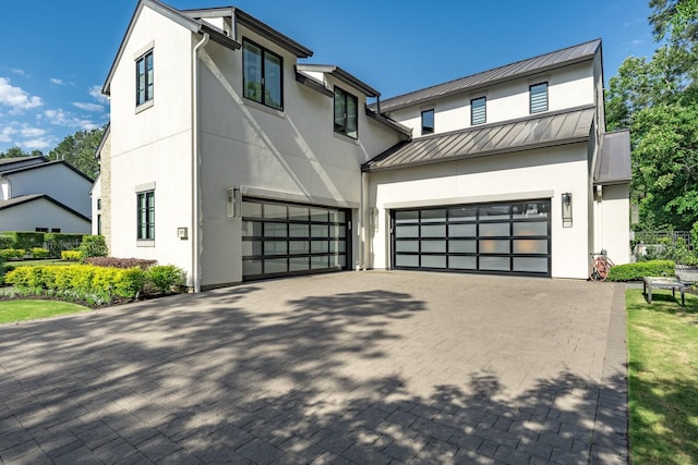 view of front of house featuring decorative driveway, a garage, a standing seam roof, and stucco siding