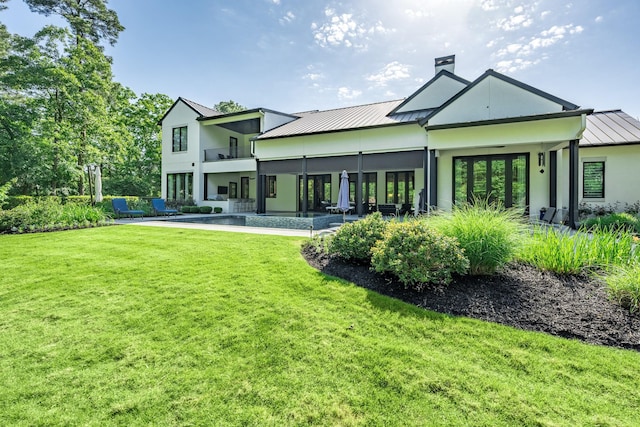 rear view of house featuring a yard, a standing seam roof, a chimney, and metal roof