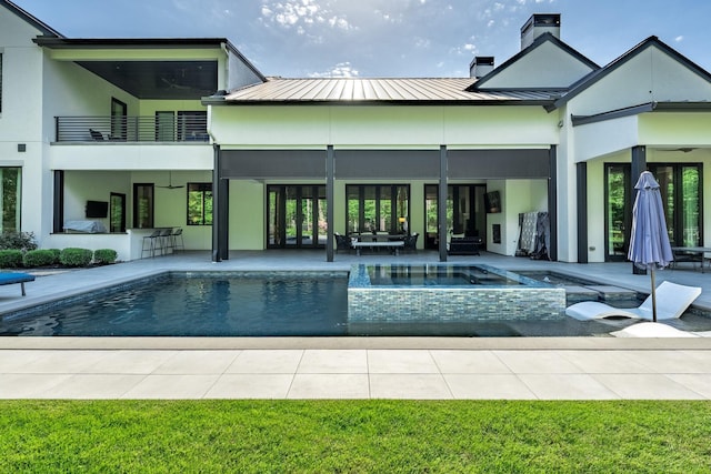 back of property with stucco siding, ceiling fan, a chimney, a balcony, and a patio