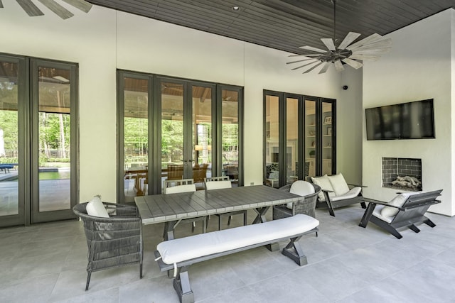 view of patio with french doors, a ceiling fan, outdoor dining space, and exterior fireplace