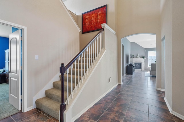 stairway featuring tile patterned flooring, a fireplace, arched walkways, baseboards, and a towering ceiling