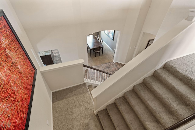 staircase with carpet floors, arched walkways, and baseboards
