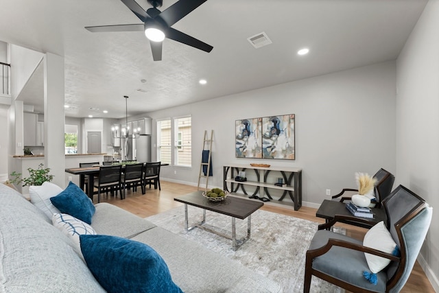 living area featuring visible vents, baseboards, ceiling fan with notable chandelier, light wood-style floors, and recessed lighting