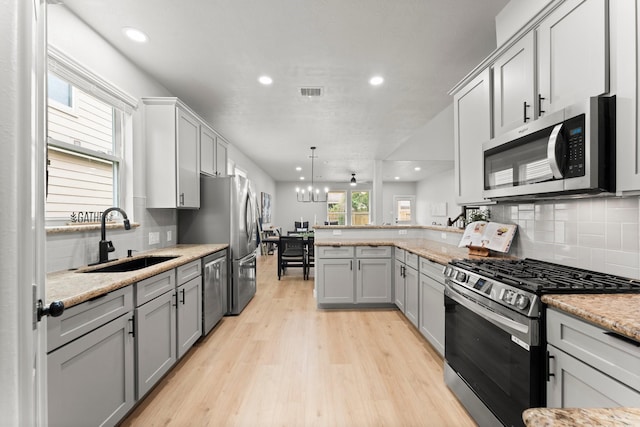 kitchen featuring appliances with stainless steel finishes, a sink, a peninsula, backsplash, and gray cabinetry