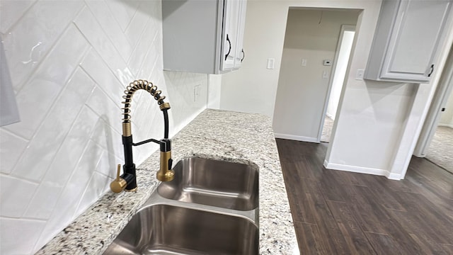 interior details with tasteful backsplash, light stone countertops, a sink, baseboards, and dark wood-type flooring