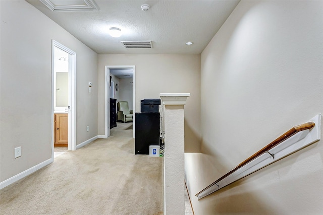 corridor with visible vents, a textured ceiling, baseboards, and light carpet