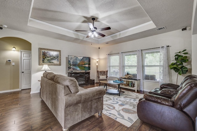 living area featuring a raised ceiling, a ceiling fan, arched walkways, and a textured ceiling