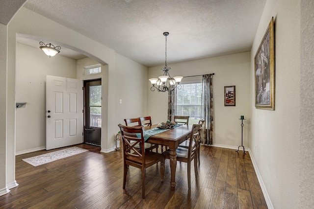 dining room with dark wood-style flooring, a notable chandelier, arched walkways, a textured ceiling, and baseboards