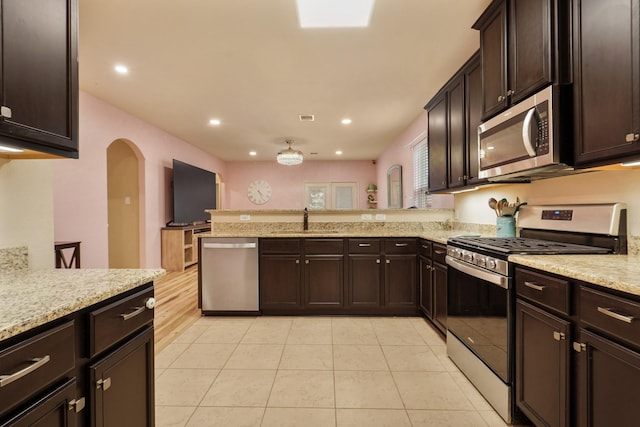 kitchen featuring appliances with stainless steel finishes, arched walkways, a sink, light tile patterned floors, and a peninsula