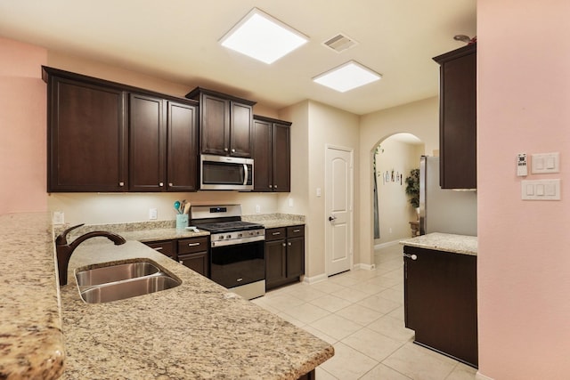 kitchen featuring visible vents, appliances with stainless steel finishes, arched walkways, dark brown cabinets, and a sink