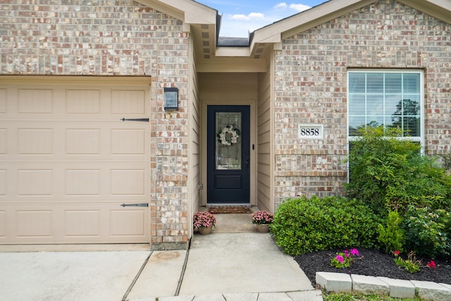 property entrance featuring an attached garage, driveway, and brick siding