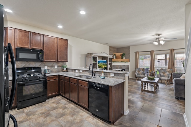 kitchen featuring a large fireplace, a sink, black appliances, a peninsula, and open floor plan