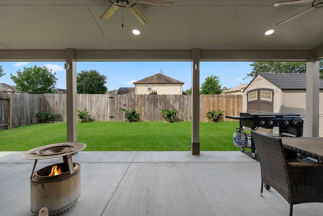 view of patio / terrace with ceiling fan, a storage shed, an outbuilding, a fenced backyard, and a fire pit