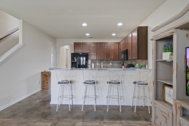 kitchen with a breakfast bar, a peninsula, recessed lighting, tasteful backsplash, and black appliances