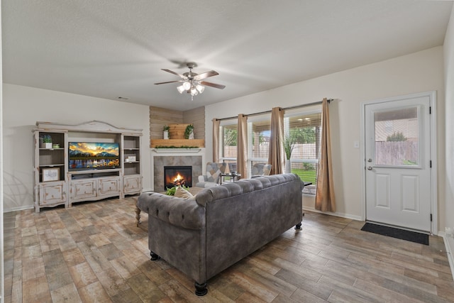 living area featuring ceiling fan, visible vents, a tiled fireplace, wood finished floors, and baseboards