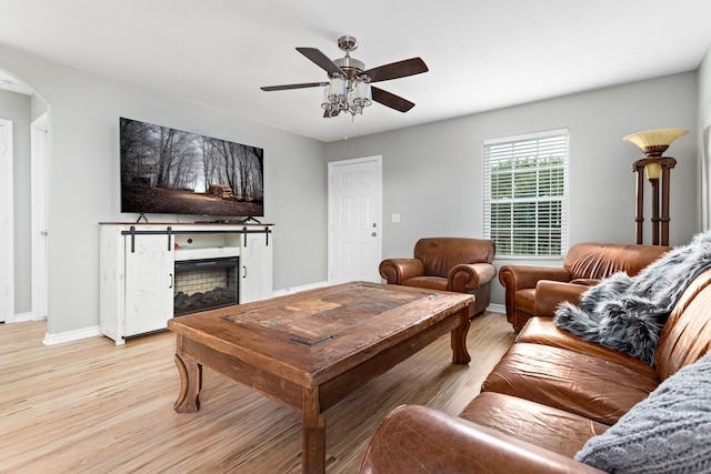living area with light wood finished floors, a fireplace, arched walkways, a ceiling fan, and baseboards