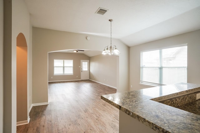 unfurnished dining area with arched walkways, baseboards, visible vents, and wood finished floors