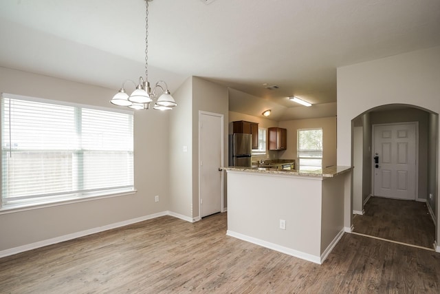 kitchen featuring light wood-style floors, freestanding refrigerator, baseboards, and arched walkways