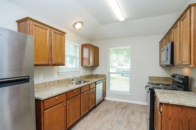 kitchen with a sink, brown cabinetry, stainless steel appliances, and light wood-type flooring