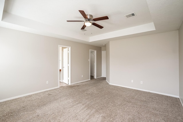 unfurnished room featuring visible vents, a ceiling fan, a tray ceiling, and light colored carpet
