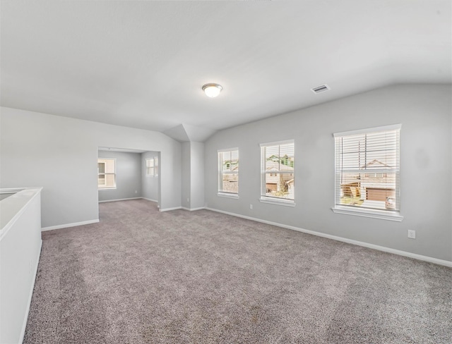 carpeted empty room with baseboards, visible vents, and lofted ceiling