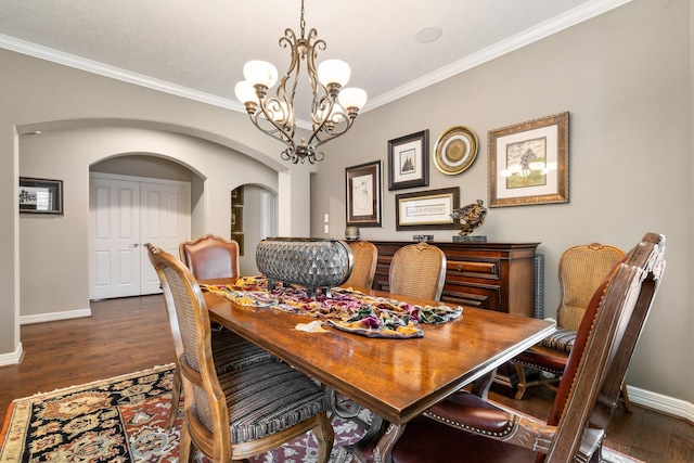 dining space with crown molding, baseboards, dark wood-style floors, arched walkways, and a notable chandelier